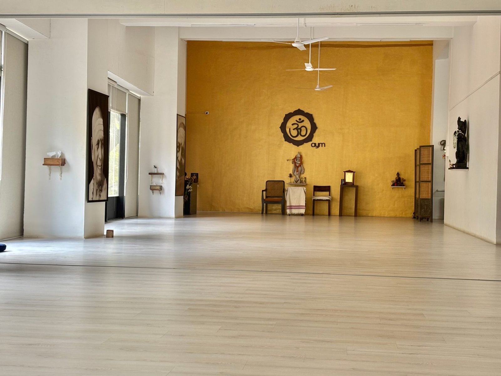 The AYM shala hall with a wooden floor, tall windows and the aym mark on a golden wall